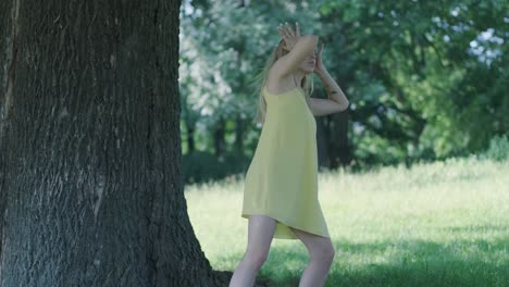 woman in yellow dress dancing by tree in summer park