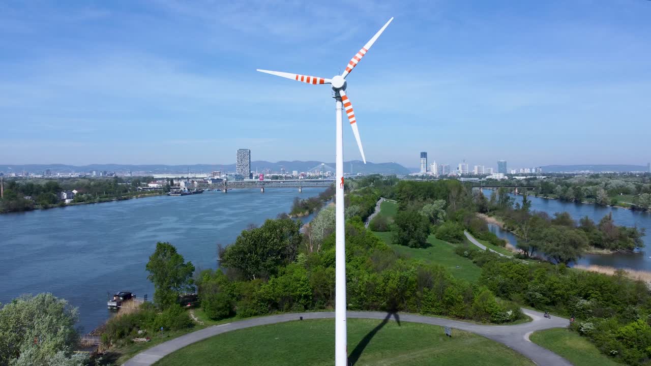 드론이 왼쪽에서 오른쪽으로 회전하여 오스트리아 비엔나의 도나우 섬에 위치한 공원의 한가운데에 있는 풍차를 보여줍니다.