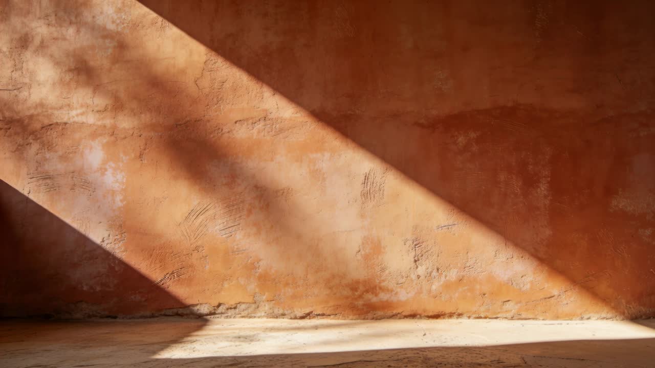 Un raggio di sole che si sposta forma un cuneo sulla parete e sul pavimento della stanza, proiettando ombre tenui mentre il sole si muove.