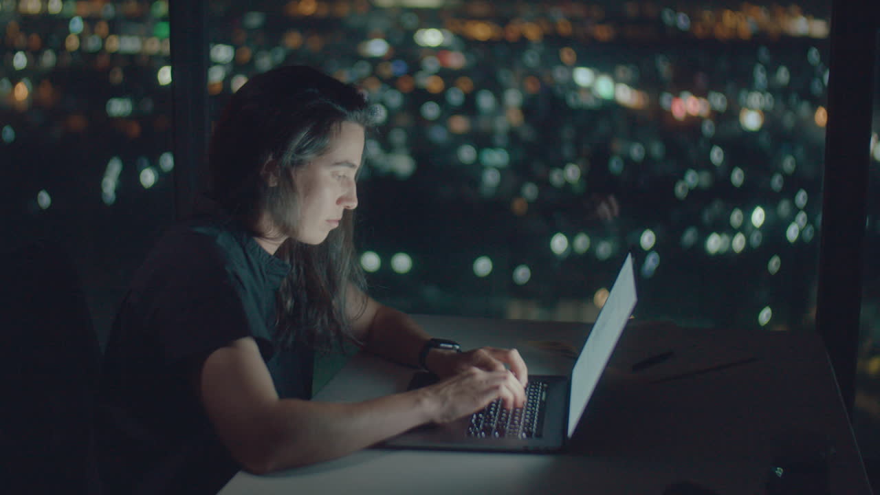 European woman typing text at night illuminated by screen