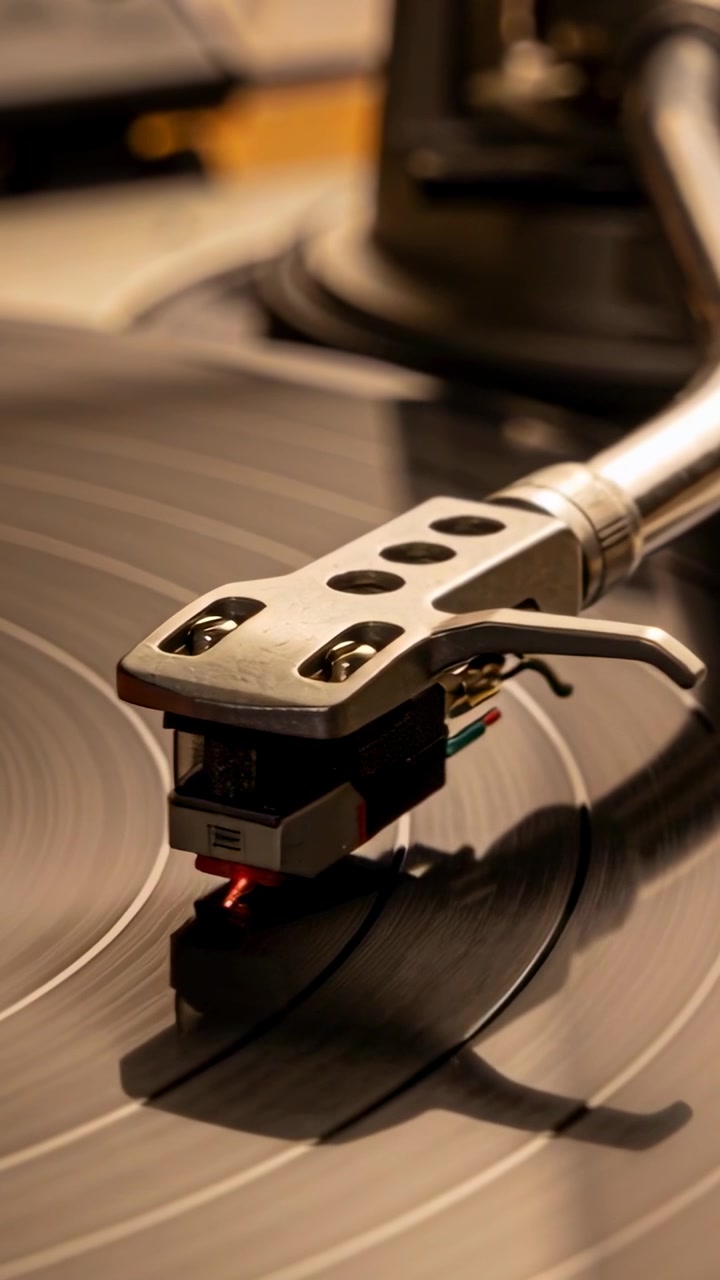 Video verticale: Un braccio e una puntina che si muovono e si posizionano nel solco di un vinile, mentre il disco gira sul piatto, con un LED rosso.