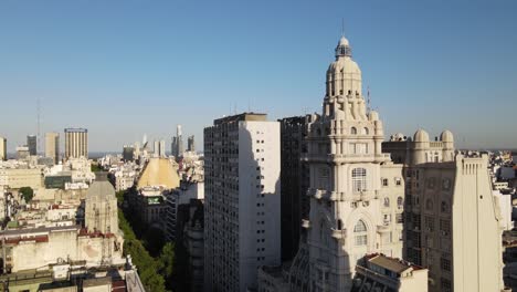 aerial dolly out of barolo palace tower and tree-lined avenida de mayo surrounded by buenos aires buildings at sunset