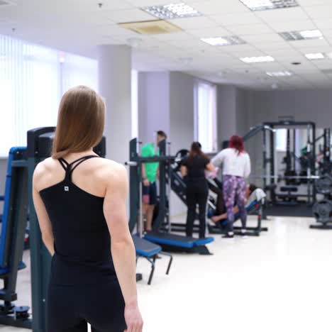 Athletic woman with her back is going to the simulator in the gym on the background of other people. Healthy lifestyle