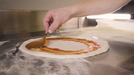 vista ravvicinata delle mani di uno chef che spalmano la salsa sull'impasto della pizza su un piano di lavoro della cucina del ristorante 1