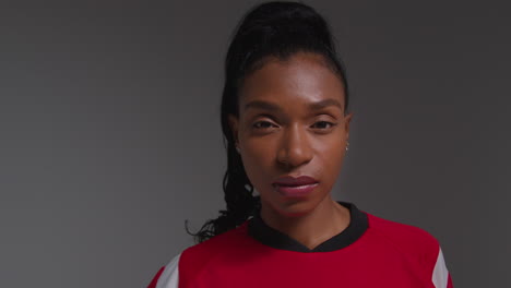 Studio-Portrait-Of-Serious-Female-Football-Or-Soccer-Player-Wearing-Team-Shirt-Holding-Ball-Under-Her-Arm-Shot-Against-Grey-Background-1