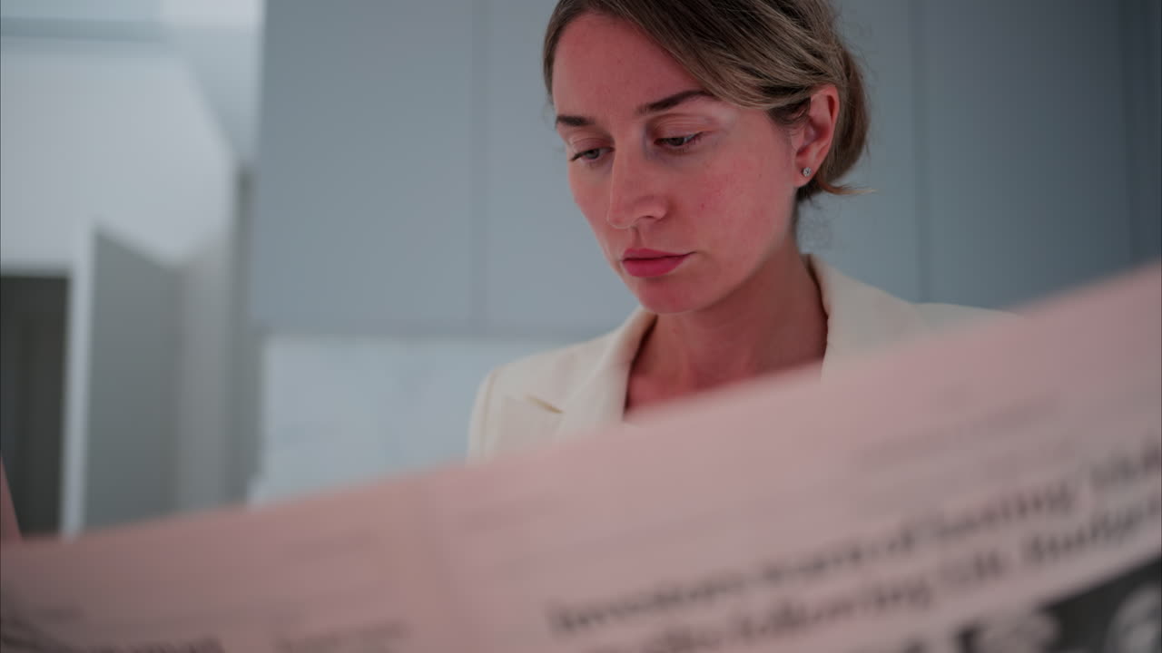 Woman in a white blazer reading the newspaper in the kitchen