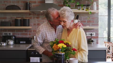 Senior-Caucasian-husband-offering-flowers-to-his-wife,-hugging-and-smiling