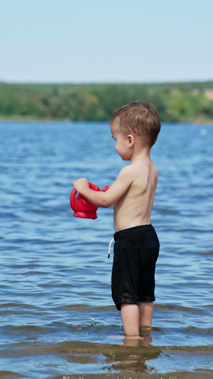 Small funny child playing on river with water. Summer sunny day and splashing on a beach. Vertical video