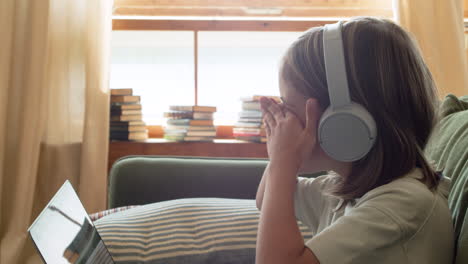 Close-Up-Of-A-Tired-Little-Girl-With-Headphones-Looking-At-The-Laptop-Screen-And-Scratching-Eyes-Out-Of-Sleep