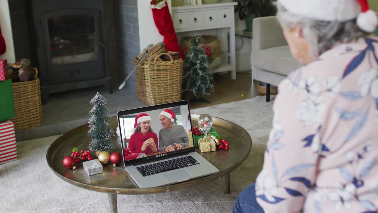 mujer caucásica mayor usando una computadora portátil para una videollamada de navidad con una familia sonriente en la pantalla