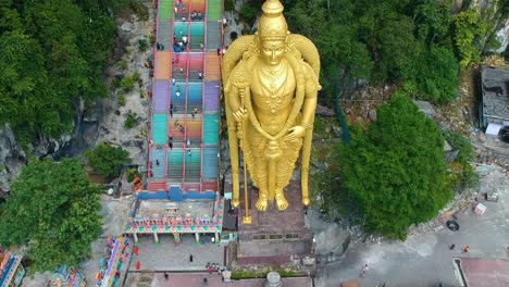 revealing aerial view of drone flying backwards recording batu caves with huge golden statue which is a hindu shrine near kuala lumpur malayasia