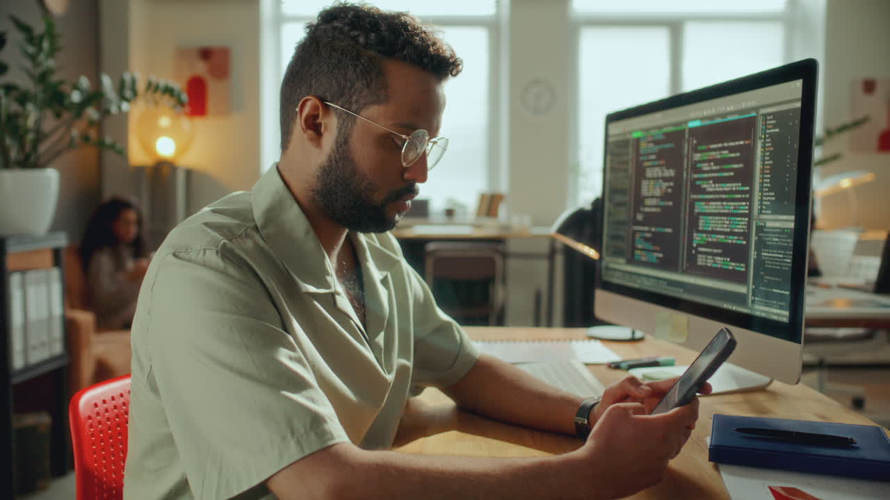 Software Developer Checking Smartphone at Desk in Modern Office
