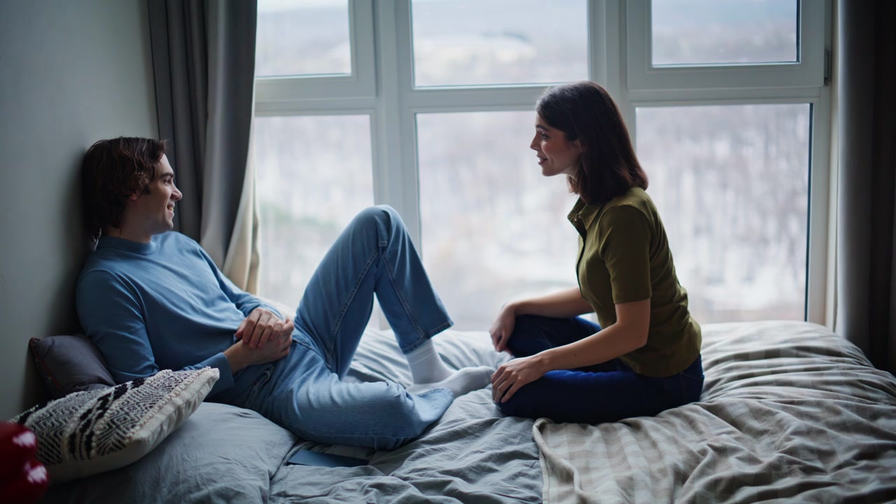 Innamorati rilassati che parlano in camera da letto, godendosi una cupa mattina di fine settimana. La coppia conversa.