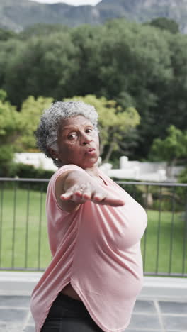 vertical video of senior african american woman practicing yoga standing on balcony, slow motion