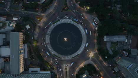 aerial birds eye overhead top down static view of vehicles driving around a busy selamat datang monument roundabout at night