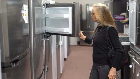 pretty mature blonde woman shopping for a refrigerator in a kitchen appliance store