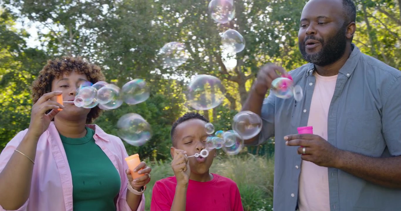 Family opening bubble bottles, dipping wands, child mimicking and blowing bubbles on lawn, bonding