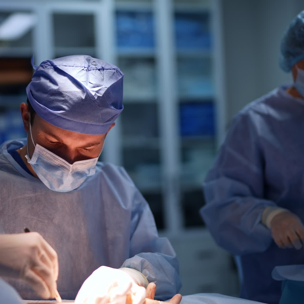 Omhyggelig kirurg, der laver et snit med skalpellen. Starten på en neurokirurgisk operation på armen. Kvindelig sygeplejerske forbereder materialer og værktøj i baggrunden