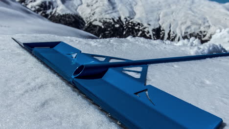 Close-up-view-of-bue-colored-triangle-snow-shaper-tool-on-snow-covered-field-in-timelapse-on-a-bright-sunny-day