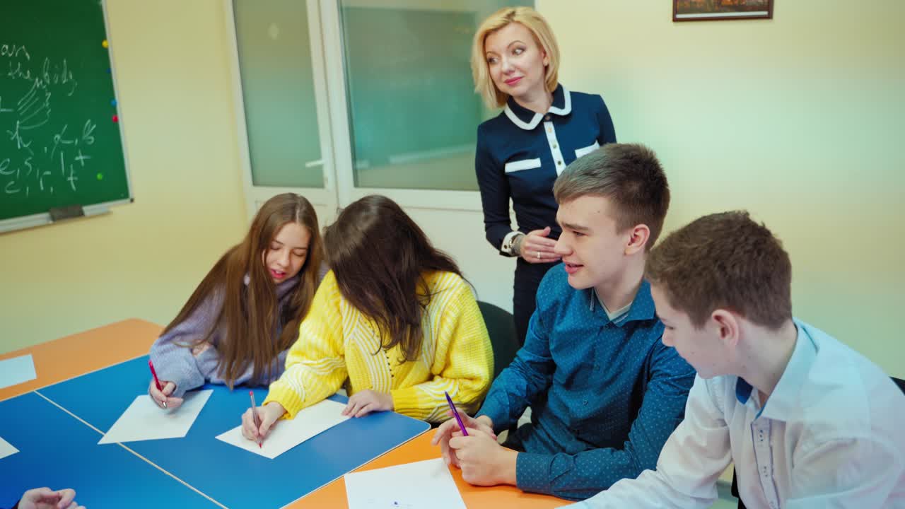 Female teacher talks with students. Teen pupils sitting in the classroom. Clever boy answering teacher questions at school.