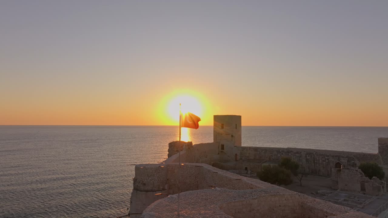 Brilho da manhã cedo sobre o Castelo da Donzela e bandeira junto ao Mediterrâneo tranquilo