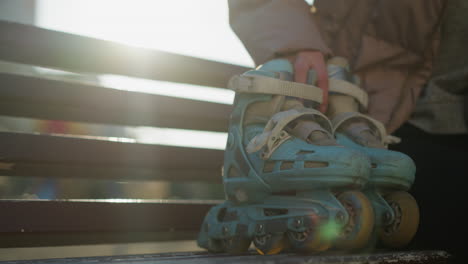 close-up shot of a person sitting on a bench, placing their rollerblades beside them, with sunlight filtering through the scene. the person then gets up and walks away, leaving the park bench