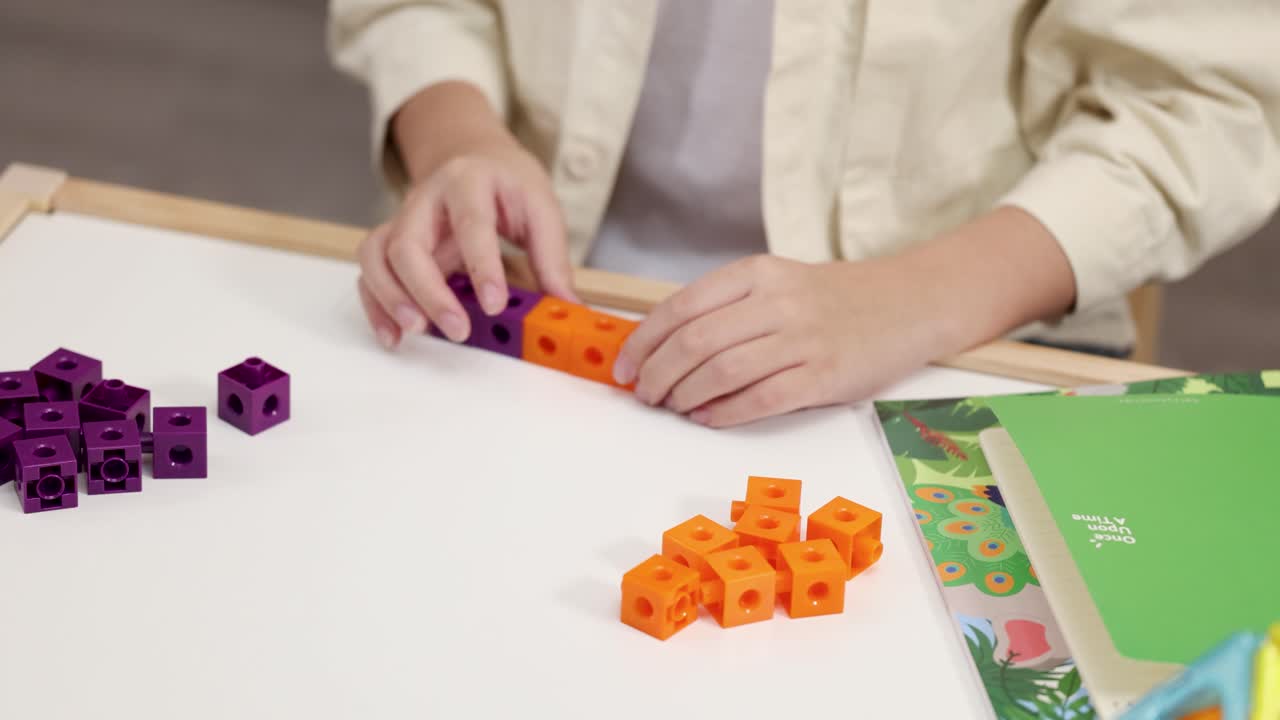 Close-up shot of a child's hands connecting orange and purple plastic cubes for math learning