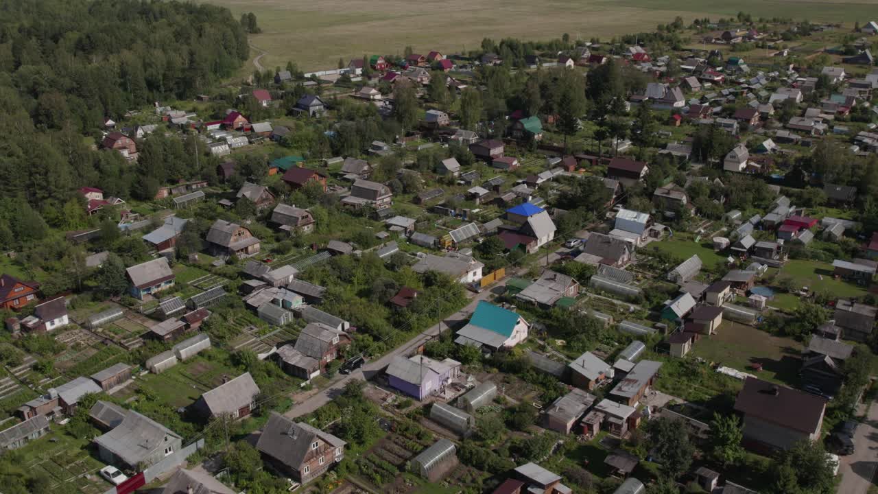 Drone footage of a small rural settlement with wooden houses, vegetable gardens and dirt roads surrounded by greenery in the Ural region, Russia during summer