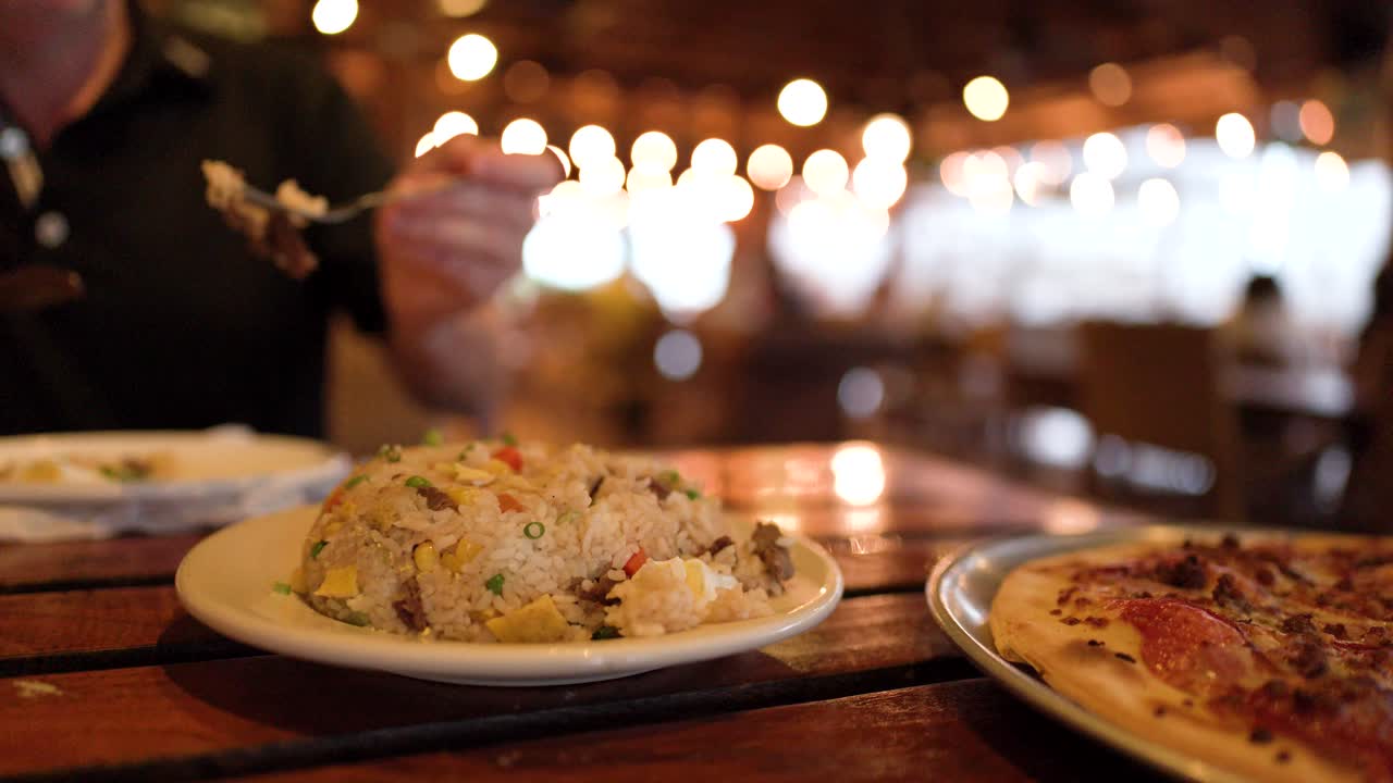 Close-up shot of a diner eating fried rice at an outdoor restaurant with bokeh lighting
