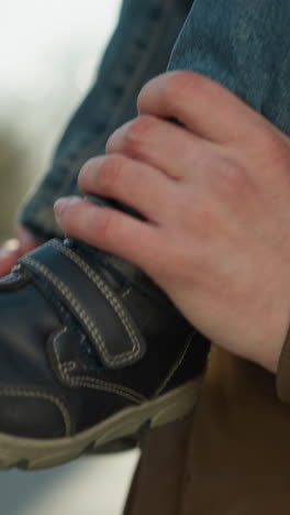 un primer plano de la mano de un adulto sosteniendo suavemente la pierna de un niño mientras son llevados en los hombros del adulto, el niño lleva vaqueros de denim y zapatos oscuros, mientras que el fondo está suavemente borroso