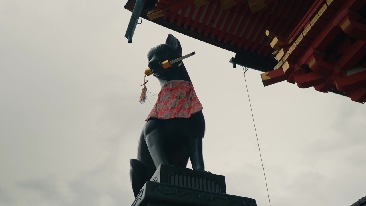 Eine geschnitzte Steinfuchs-Wächterstatue steht unter einem roten Schreindach, ein Symbol der japanischen Inari-Schreine