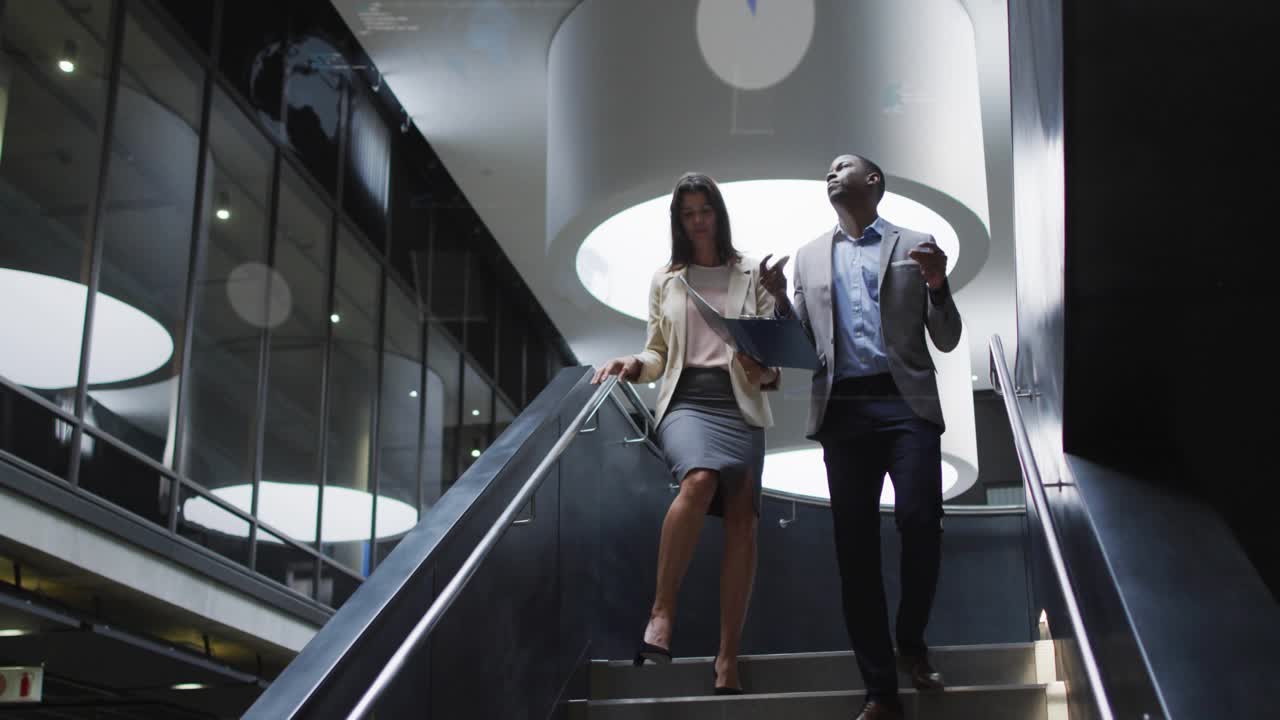 Woman holding folder starting down, man gesturing reviewing business data, blue charts overlaying