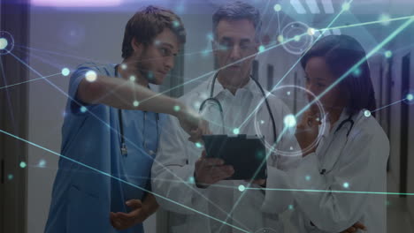 three medical team holding tablet and pointing in hospital hallway, showing glowing network lines
