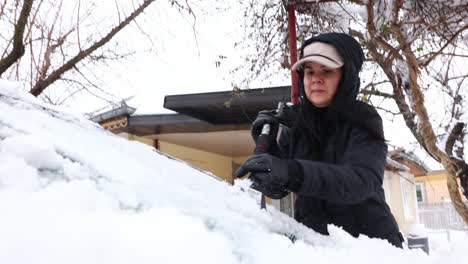 close up of woman cleaning snow from car using an ice scraper