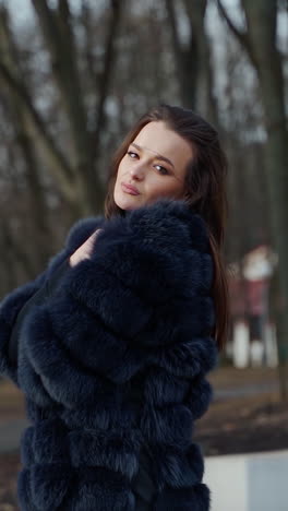 young beautiful fashionable lady wearing stylish dark fur coat posing in park. model looking aside. female fashion concept video. vertical video