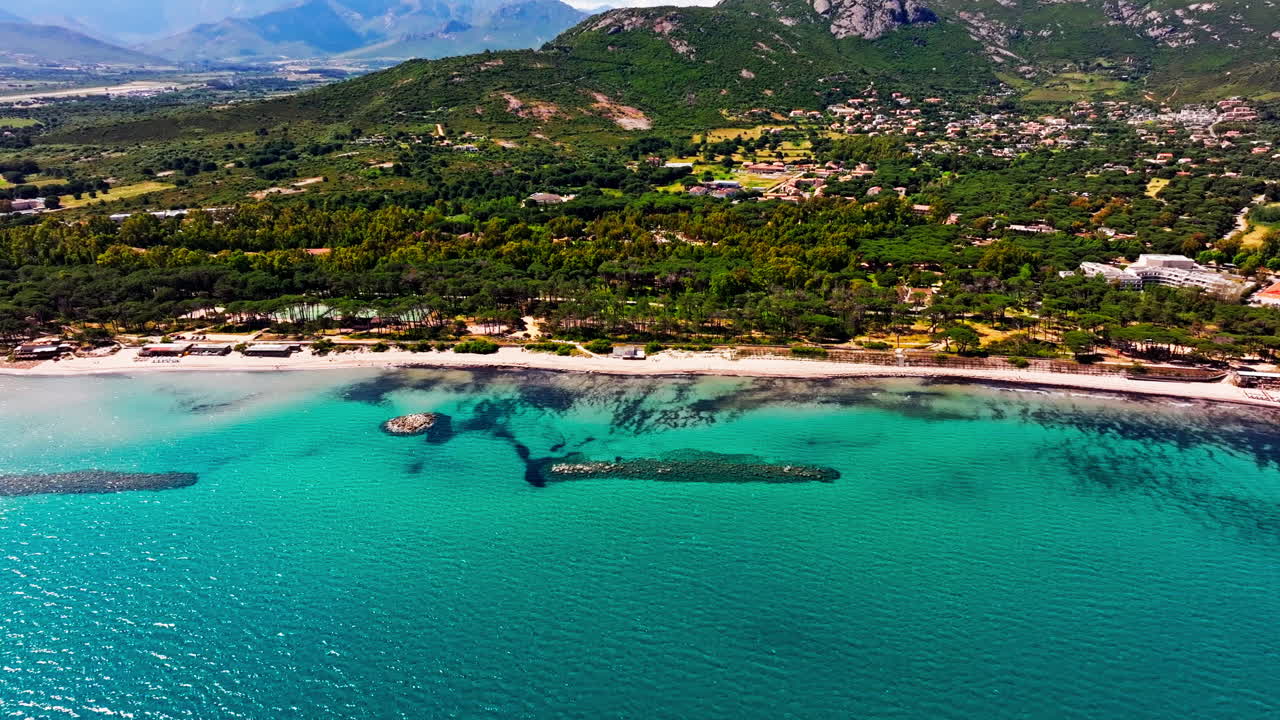 Korsika’daki bir plajın havadan drone ile çekilmiş görüntüsü. Yeşil dağların ve turkuaz denizin yüksekten görünümü. Yaz tatili destinasyonu
