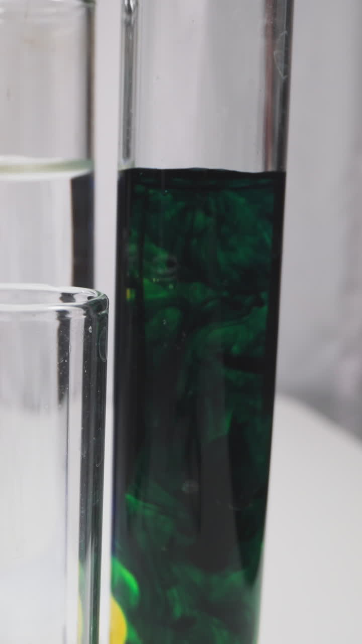 Dripping dark reagent into test tube with green liquid under lab assistant control in workshop slow motion. Probe lens shot of experiment closeup