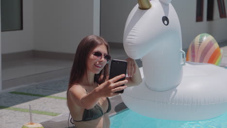 una mujer tomando una selfie en la piscina con un unicornio inflable.