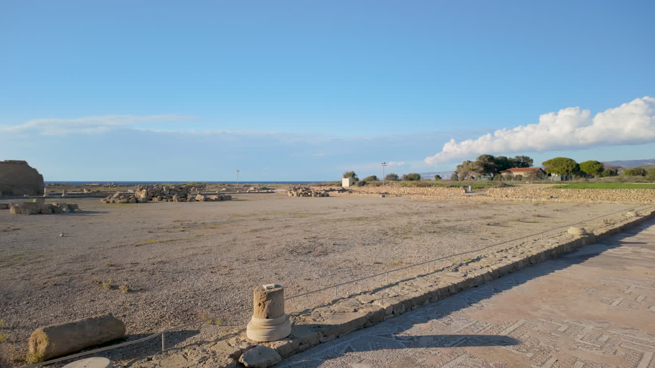 una vista expansiva de un sitio arqueológico en pafos, con antiguas ruinas y caminos de piedra bajo un cielo azul brillante