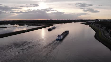 an empty barge ship passes to a tanker sailing on inland waterway during sunset