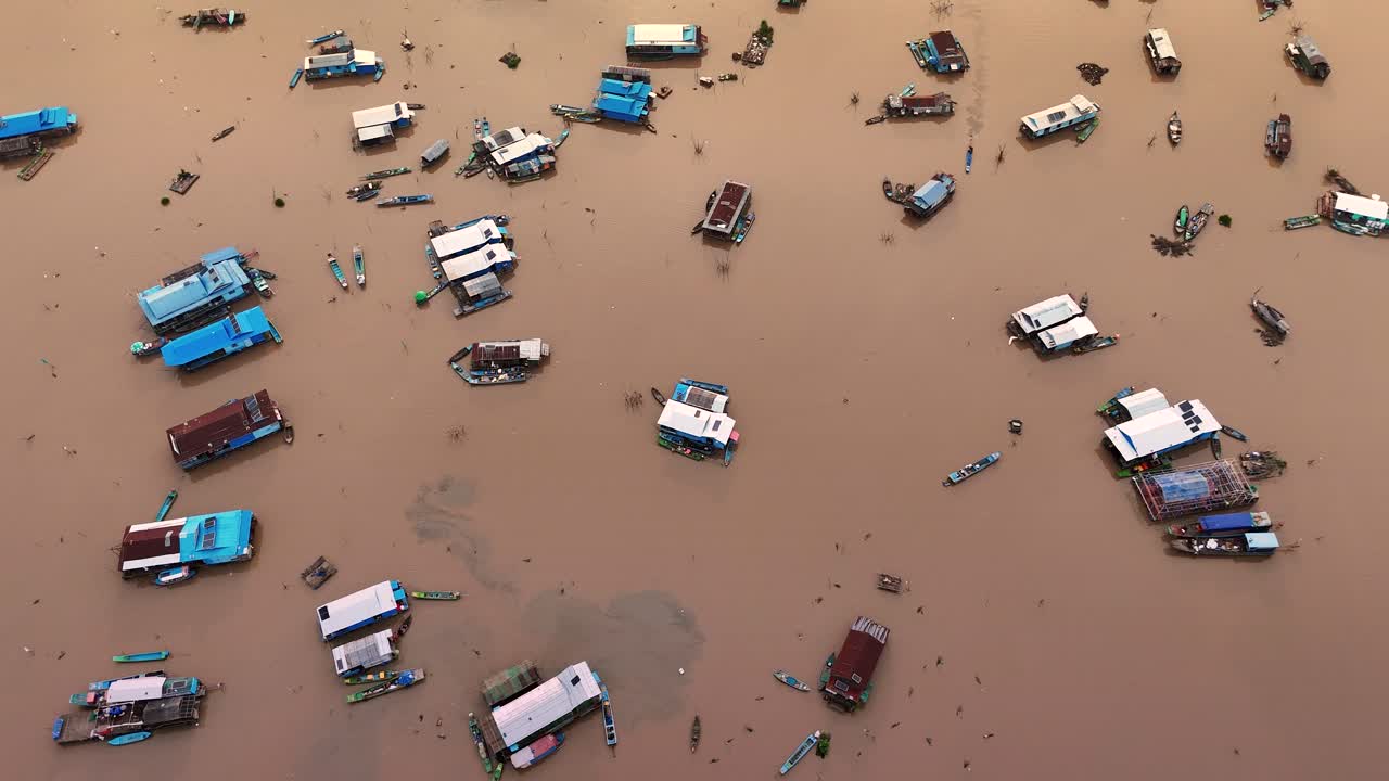 Top-down drone view of Tonle Sap’s floating village, Cambodia, with floating houses and boats scattered across the murky lake.