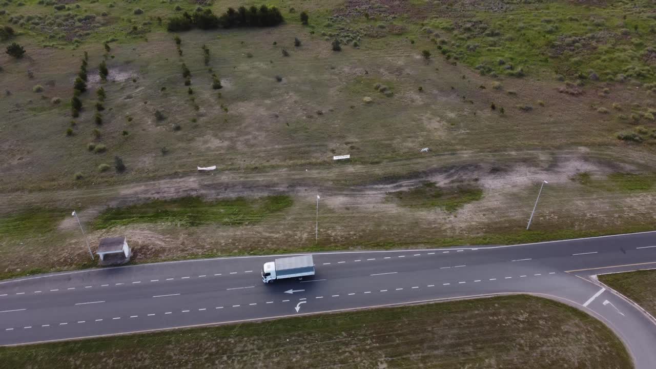 Ripresa aerea dall'alto di un camion bianco che svolta su una strada asfaltata rurale circondata da campi verdi durante il giorno