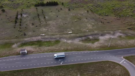 aerial top down shot of white truck turning on rural asphalt road surrounded by green fields during daytime