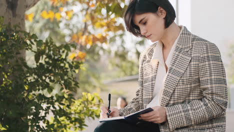 emprendedora elaborando un plan de negocios durante un mes en un bloc de notas mientras descansa al aire libre.