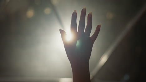 woman palm silhouette at backlight in dark room closeup. lady hand with touching gestures and glowing light in dark space. hope creative concept