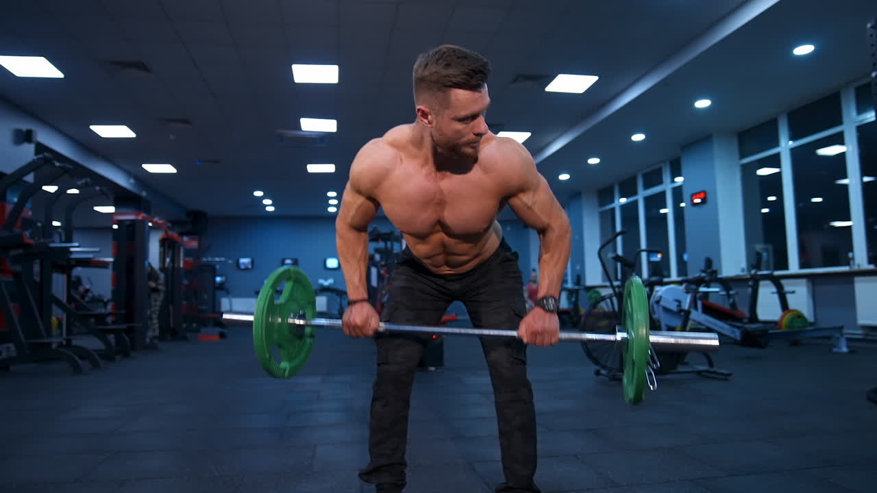 Male athlete trains with barbell in empty gym with modern equipment. Slow motion.