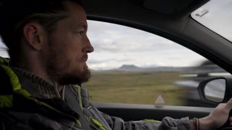 Toma-Lateral-De-Un-Hombre-Caucásico-Concentrado-Conduciendo-El-Automóvil-En-El-Paisaje-Montañoso-De-Islandia.