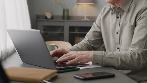 la cámara se enfoca en las manos de un anciano escribiendo en una laptop y sosteniendo una taza de café en el escritorio