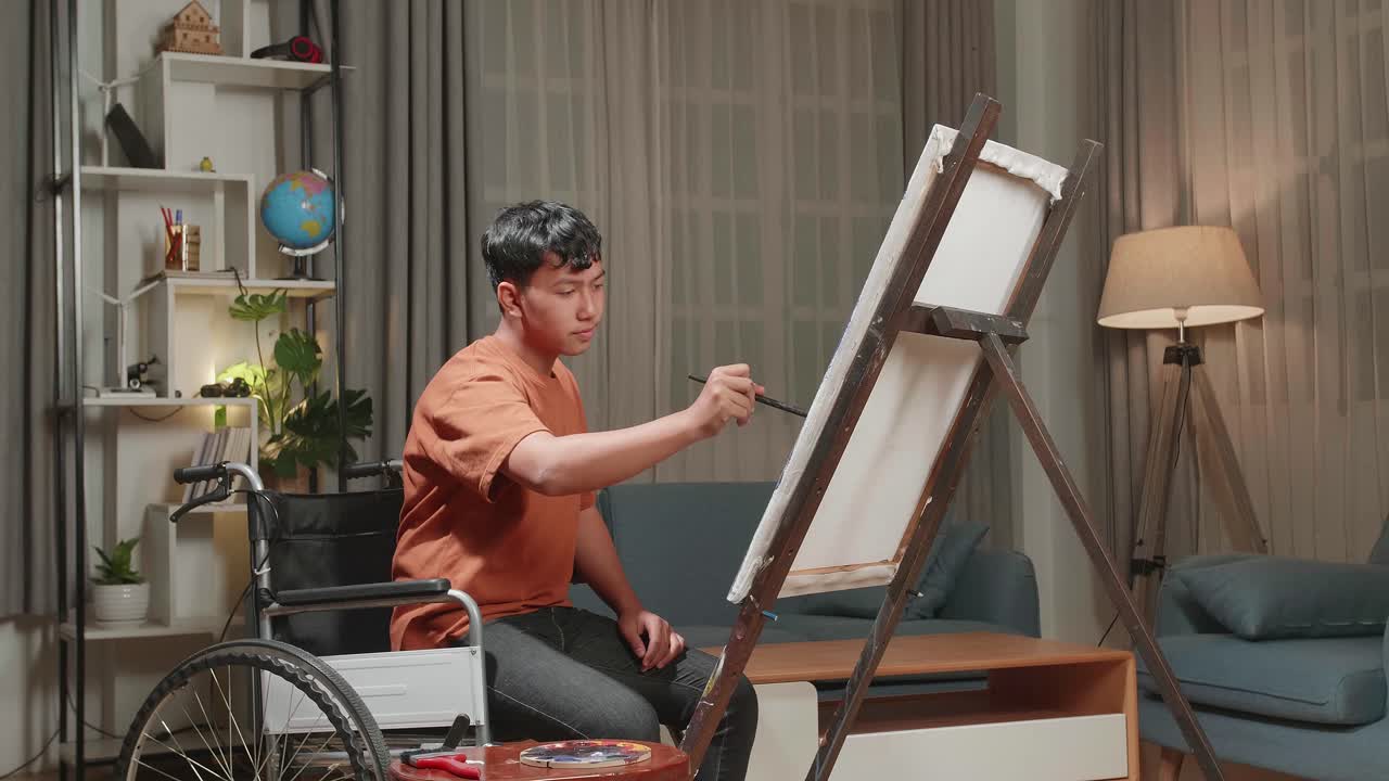 Asian Artist Boy In Wheelchair Holding Paintbrush Mixed Colour And Painting On The Canvas