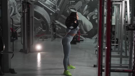 contrasting light of a sporty girl squatting with a barbell